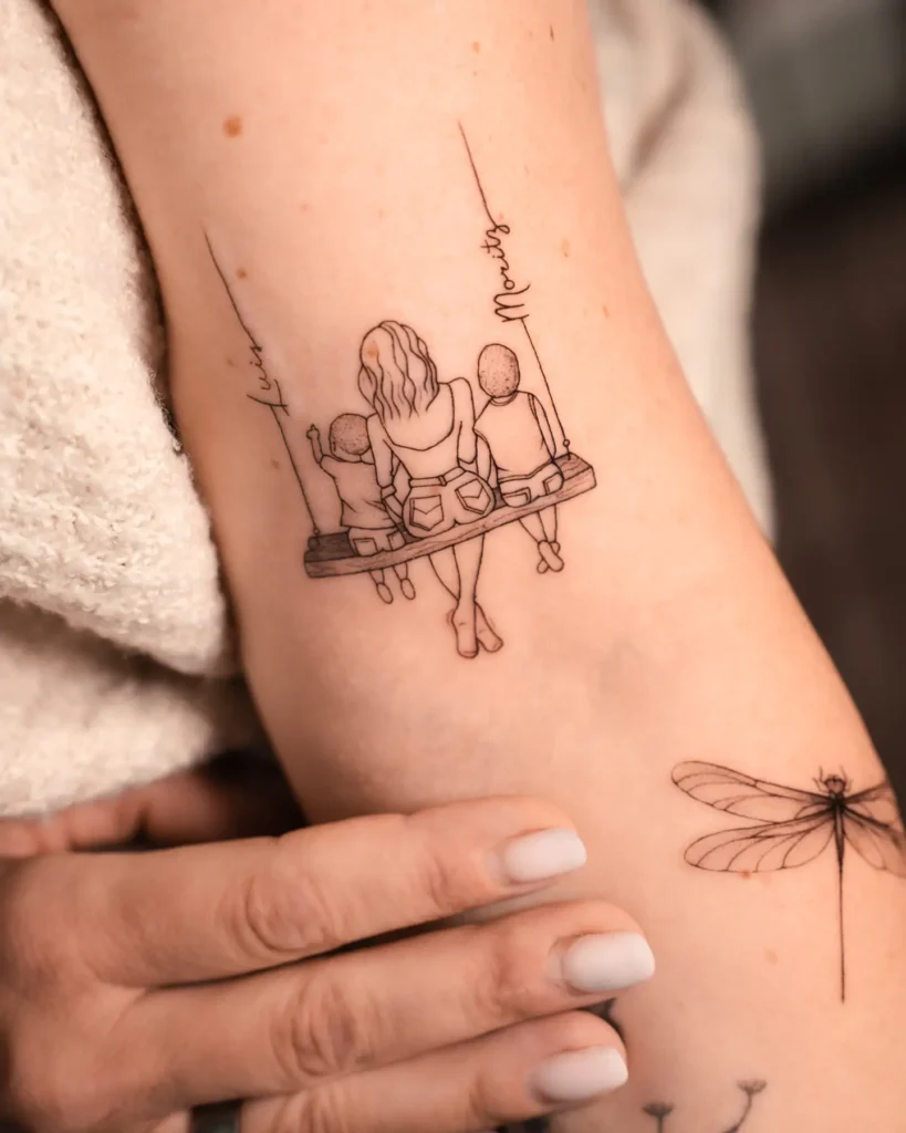 Fine line tattoo on the arm showing a mother with two children sitting side by side on a wooden swing, viewed from the back. The names “Lucas” and “Maurits” are written along the swing’s ropes, highlighting a close family bond in a minimalist, delicate style.