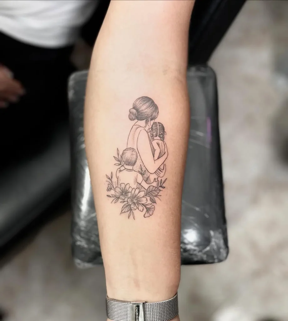 Forearm tattoo shows a mother with her hair in a bun, hugging her daughter and son. Both children face forward while flowers bloom below, framing the trio in black and grey ink. Fine linework and soft shading make this tattoo a beautiful tribute to mom and daughter tattoos unique, celebrating love and togetherness.