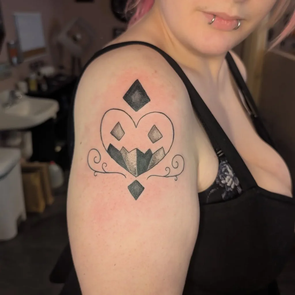 Black geometric tattoo on a woman’s upper arm, featuring a heart outline, diamonds, and bold angular patterns.