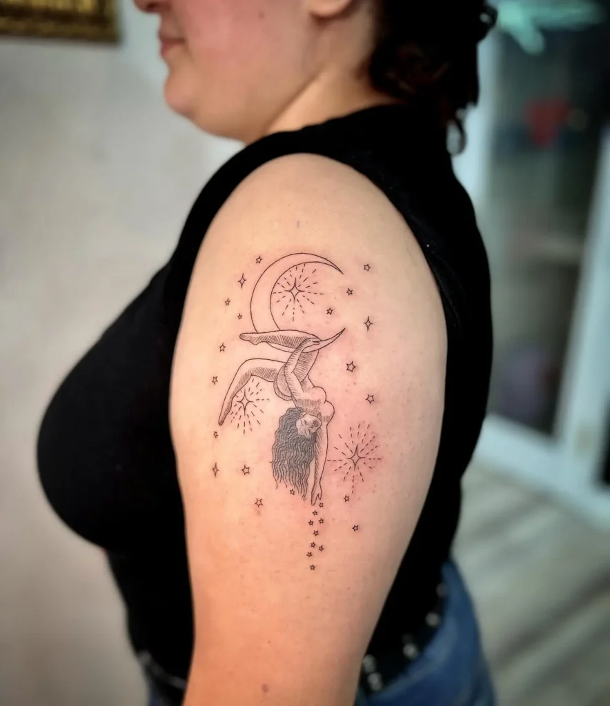 Tattoo of an acrobat hanging below a crescent moon, with stars and sparkles, inked on a woman’s upper arm.