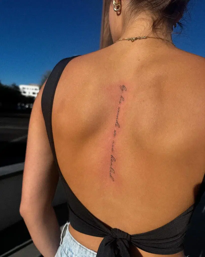 A spine tattoo with an inspirational quote in fine script, arranged vertically down a woman’s back.