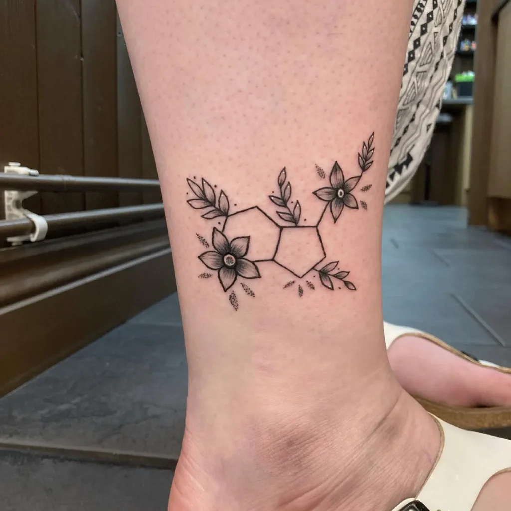 An ankle tattoo of the serotonin molecule surrounded by delicate flowers and leaves, symbolizing happiness, mental wellness, and natural beauty.