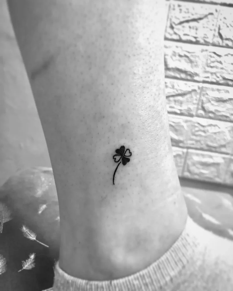 Small black clover tattoo on a woman’s ankle, featuring thin lines and minimalist style.