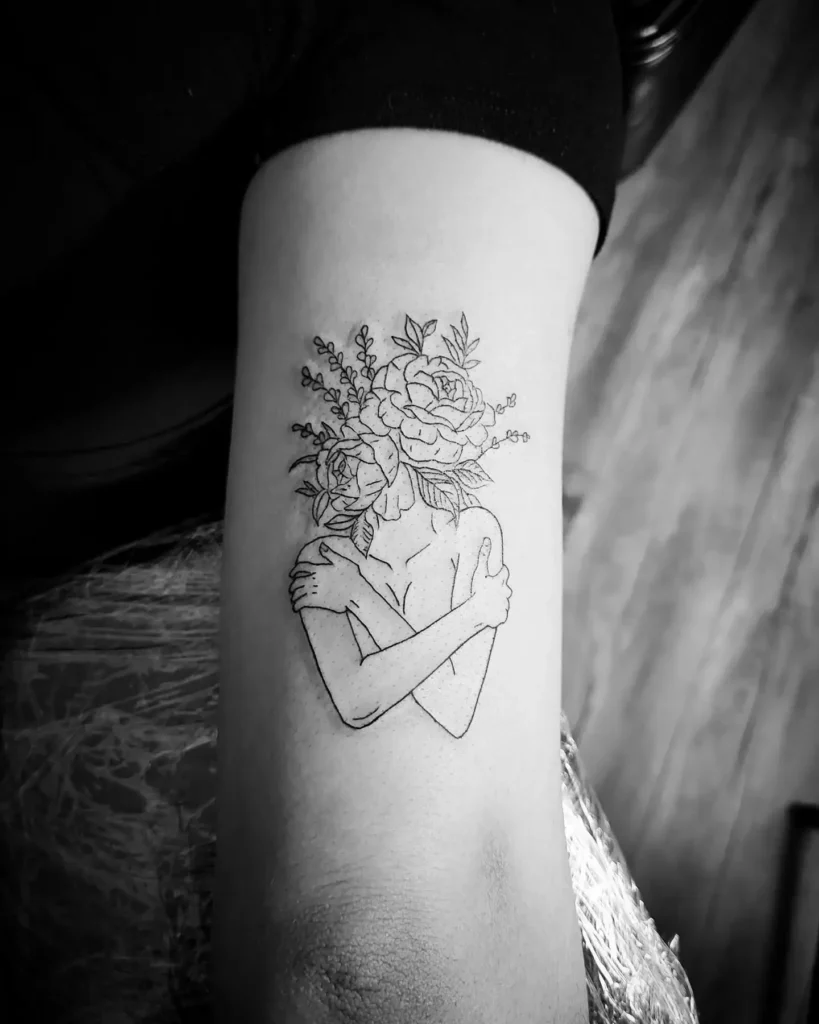A black and white tattoo of a person hugging themselves with flowers blooming from their head, symbolizing self-love, healing, and personal growth.