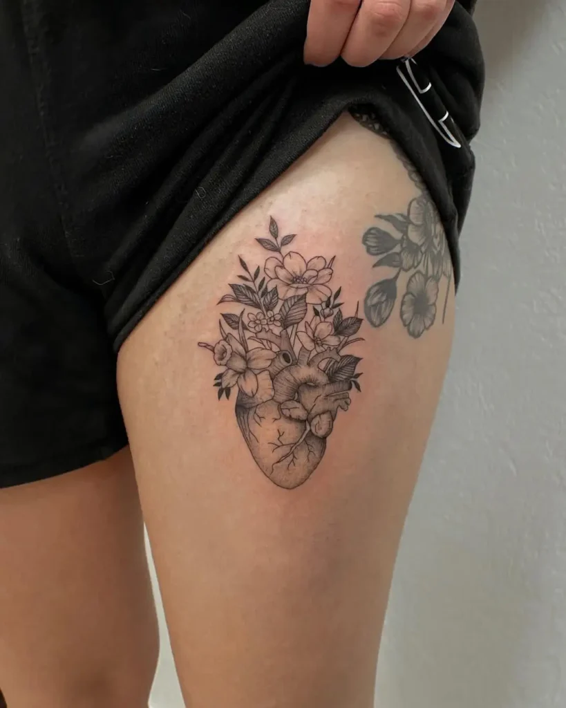 Fine line thigh tattoo of an anatomical heart sprouting wildflowers, symbolizing emotional depth, growth, and inner resilience.










