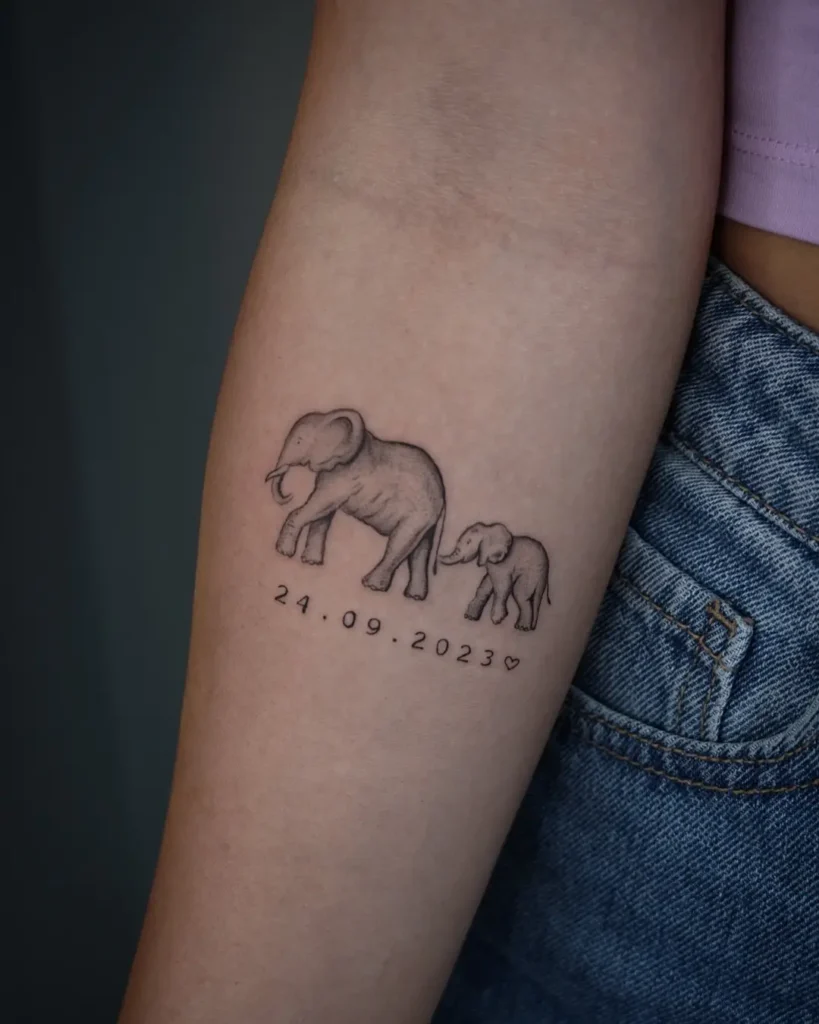 Minimal elephant tattoo showing a large and small elephant holding trunks with a date “24.09.2023” beneath. Placed on the inner arm near the elbow. Represents love, memory, and bond. A perfect example of animal tattoo ideas easy, simple, and personal—ideal for forearm placement with sentimental meaning.








