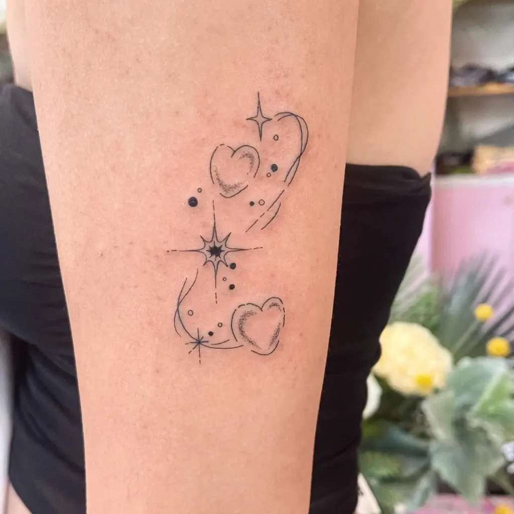 Fine line tattoo of two shaded hearts with sparkles and swirl lines, symbolizing joy, connection, and delicate beauty on the upper thigh.










