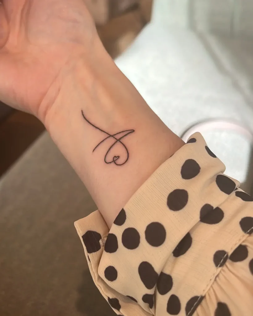Minimalist black line tattoo forming a looping script with a small heart on a woman’s inner wrist.