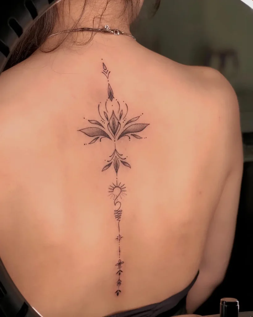 An ornamental lotus spine tattoo with fine-line details, leaves, and sunburst accents on a woman’s back.