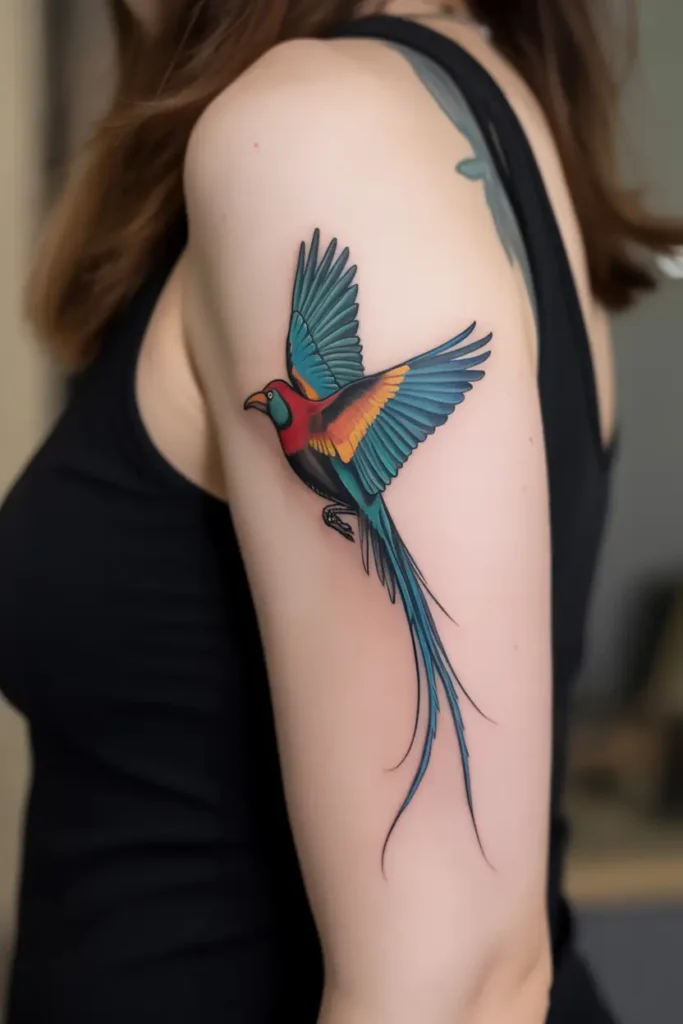 Colorful quetzal bird tattoo on upper arm with long tail feathers, inspired by traditional Mexican tattoo ideas and vibrant cultural symbolism.