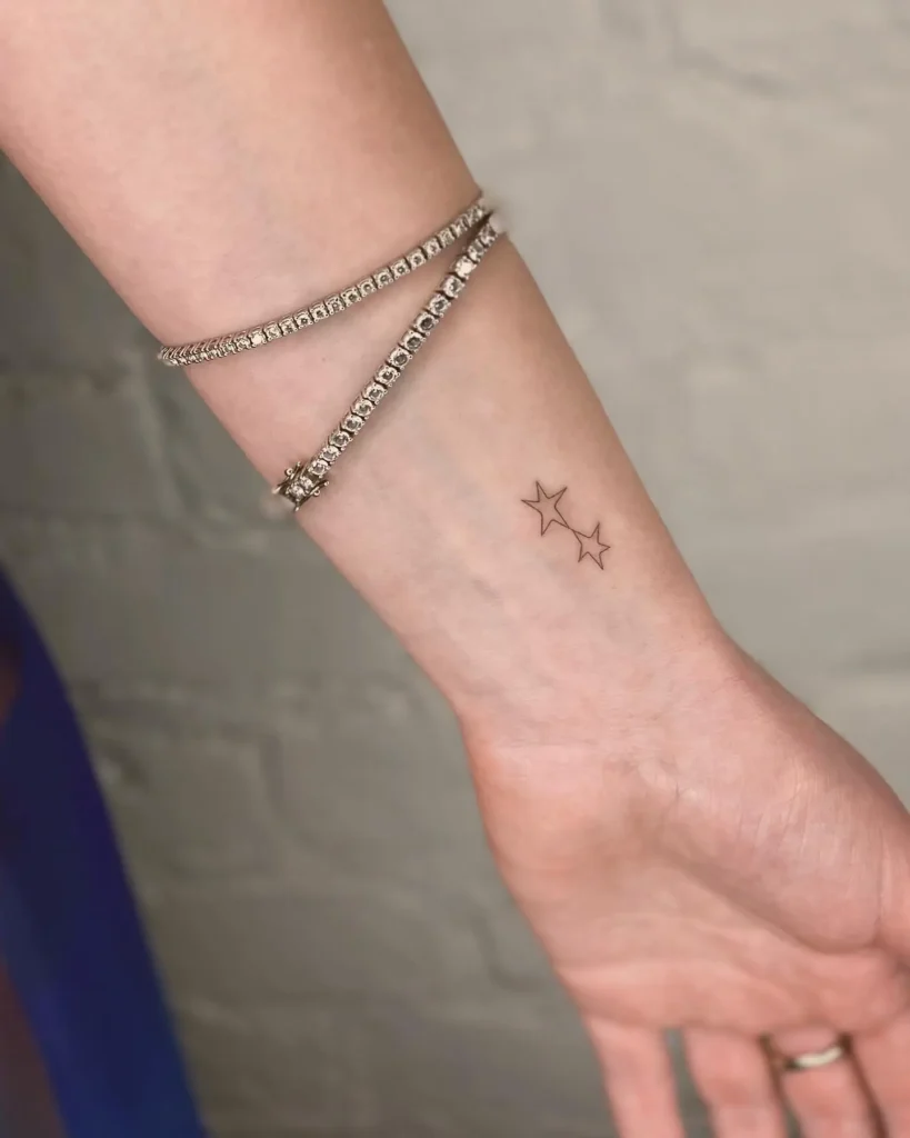Two small black star outline tattoos inked on the inner forearm of a woman’s arm.