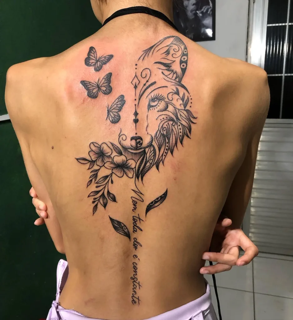 Large back tattoo featuring a stylized wolf face formed with floral and tribal linework, paired with butterflies and Portuguese script “Nem toda dor é constante.” Designed in fine black ink with elegant flow and detailed curves. Powerful choice for animal tattoo ideas sleeve-style on the back, combining symbolism of healing, strength, and transformation.








