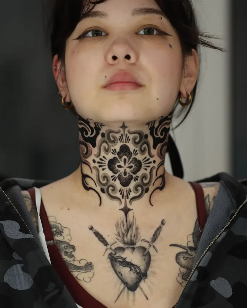 Bold ornamental mandala throat tattoo for women, symmetrical neck design with black shading and decorative lace-like pattern.