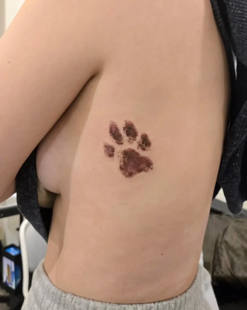 Watercolor dog tattoo featuring a joyful dog’s face with blue, pink, and orange accents, surrounded by soft floral details on light skin.