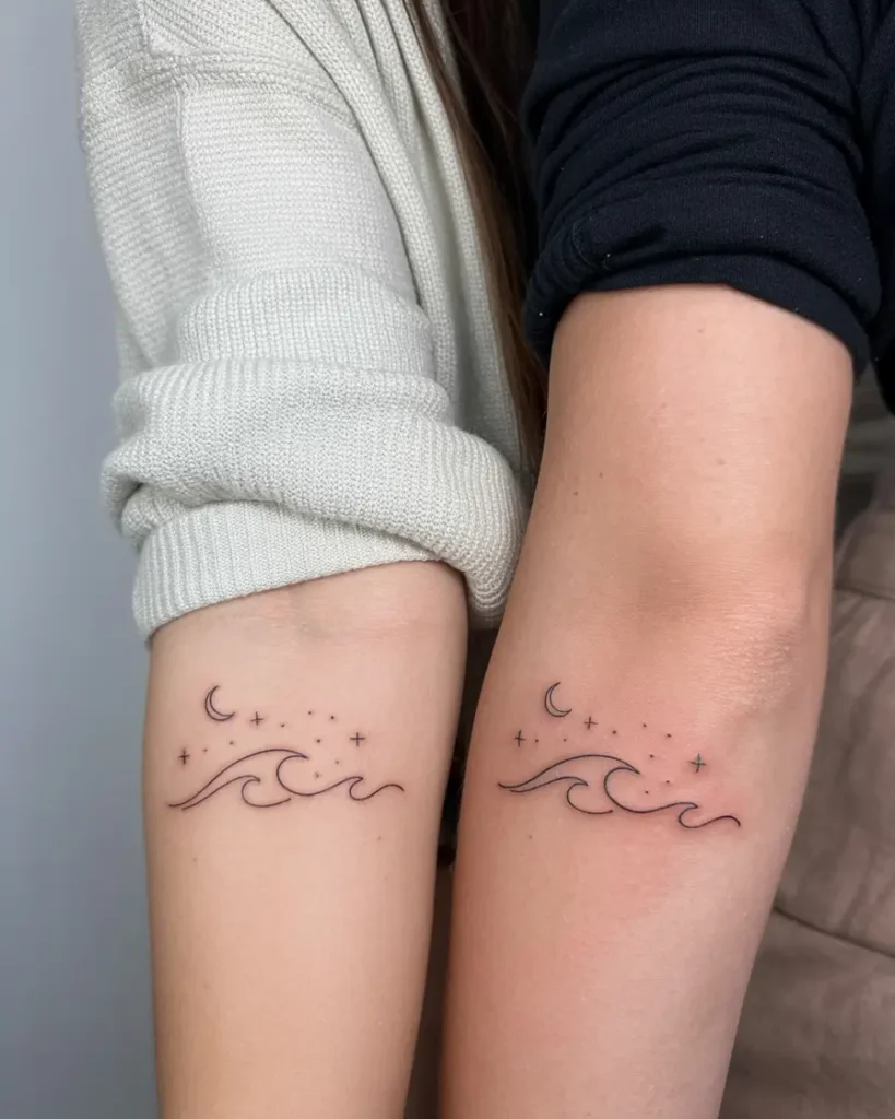 Close-up of two forearms, each with a small matching tattoo showing flowing waves, a crescent moon, and scattered stars above. The design uses thin black lines for a minimal look. This tattoo celebrates mom and daughter tattoos unique by using celestial and ocean elements to symbolize connection, peace, and shared life journeys.