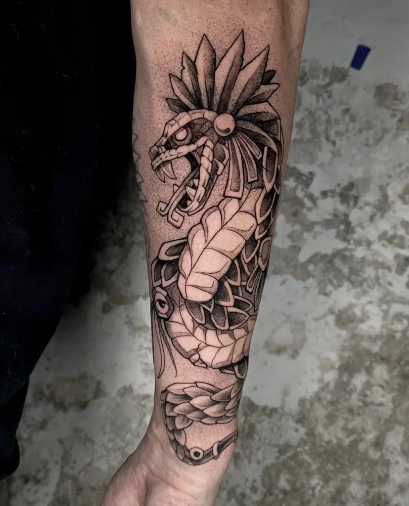 Black and gray forearm tattoo of Quetzalcóatl, the Aztec feathered serpent god, featuring bold linework and detailed shading inspired by traditional Mexican tattoo art.