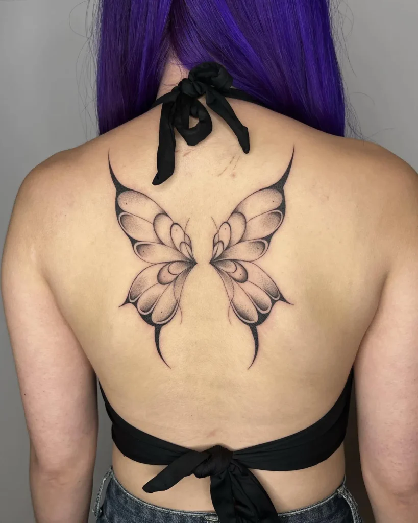 Large symmetrical butterfly tattoo on upper back with sharp edges and gradient shading, bold fine line design for women.









