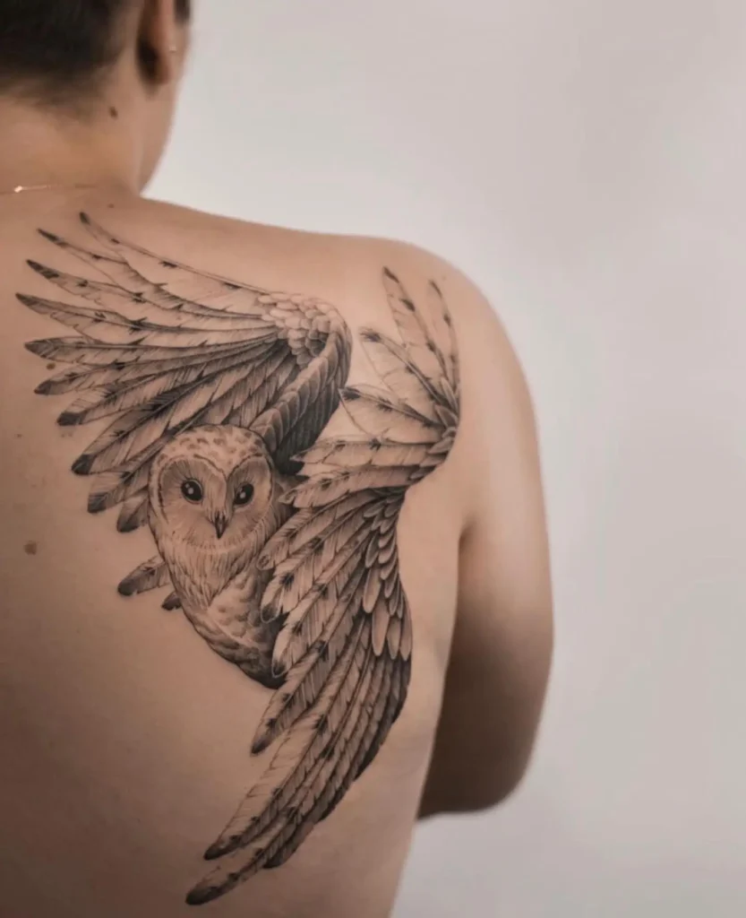 Large back tattoo of a flying owl with wide, detailed wings in black and grey ink. Positioned across the shoulder blade, feathers drawn with fine realism and motion. Symbolizes wisdom, clarity, and freedom. A graceful choice among animal tattoo ideas sleeve-alternatives with meaningful, nature-inspired elegance.








