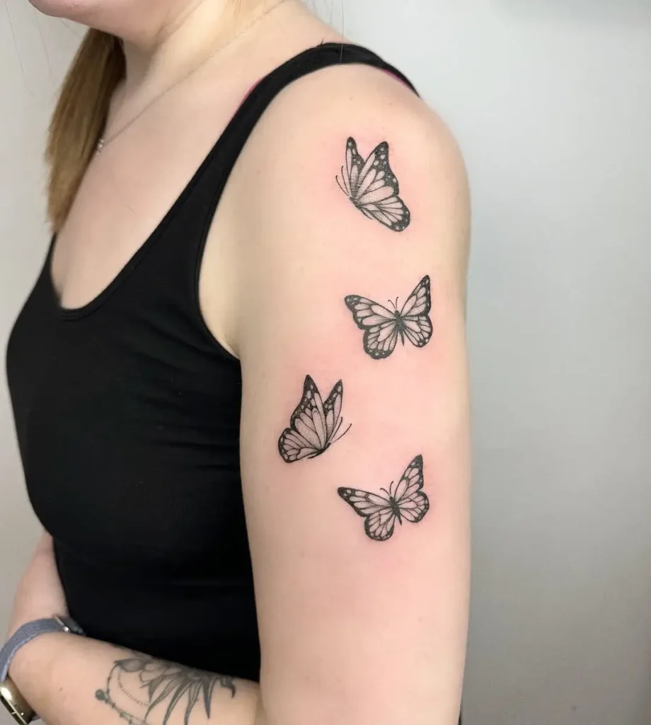 Three fine line butterflies tattooed on upper arm with soft shading and dotwork, minimalist butterfly tattoo design for women.









