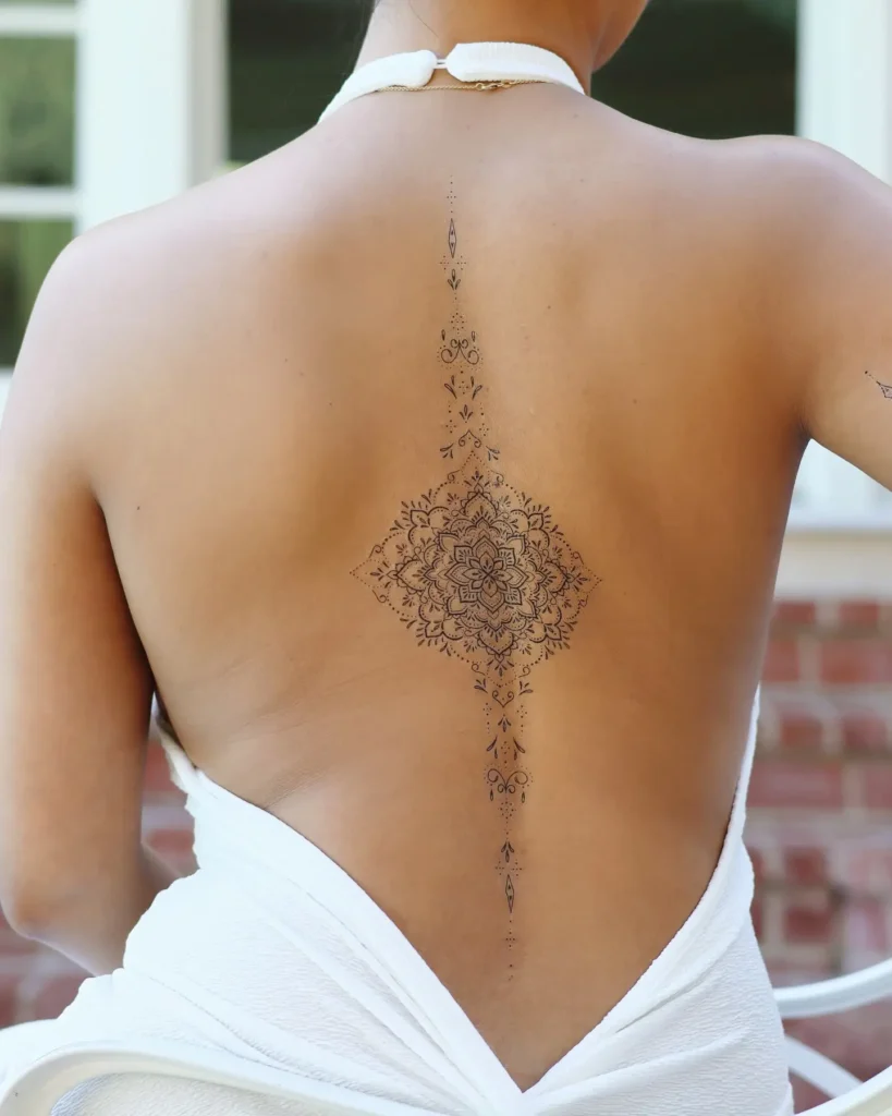 A diamond-shaped mandala spine tattoo with fine-line accents, centered on a woman’s back.