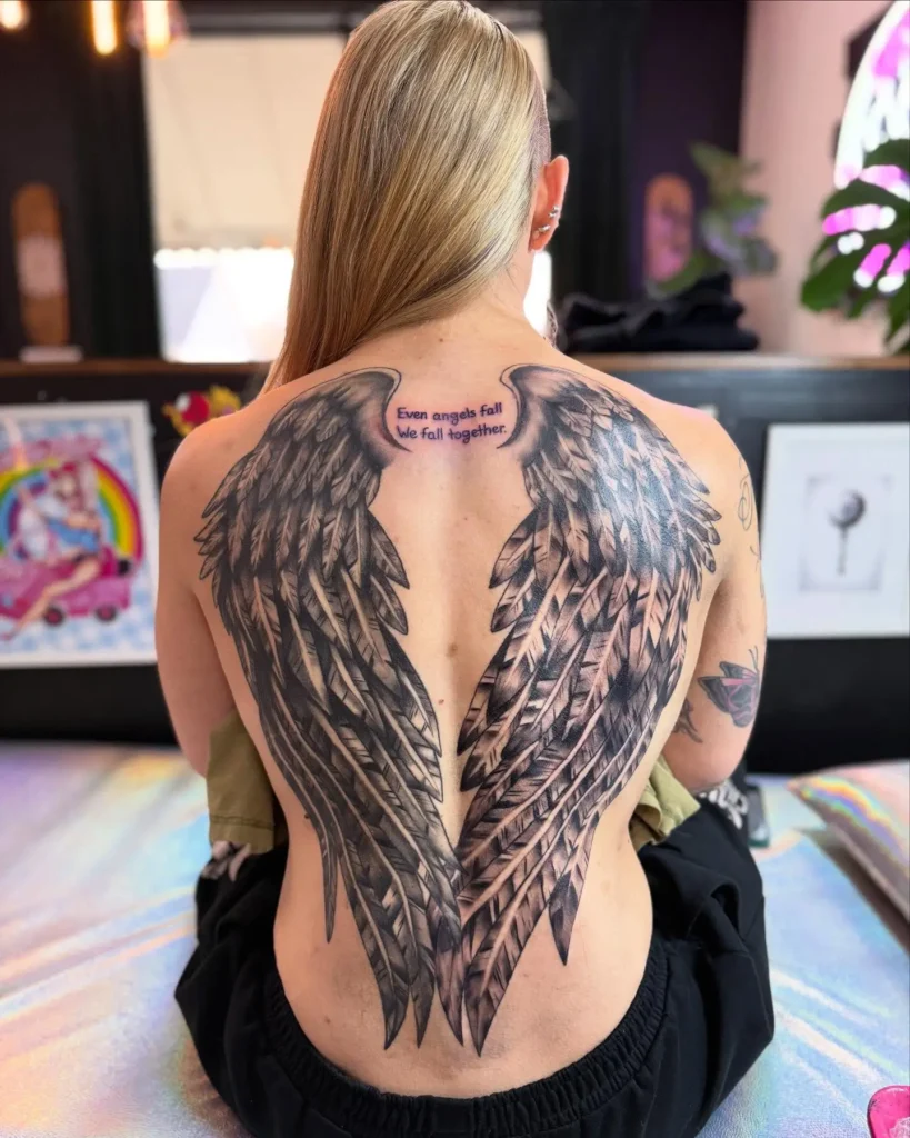 Full-back angel wings tattoo with quote “Even angels fall. We fall together,” symbolizing strength and emotional connection

