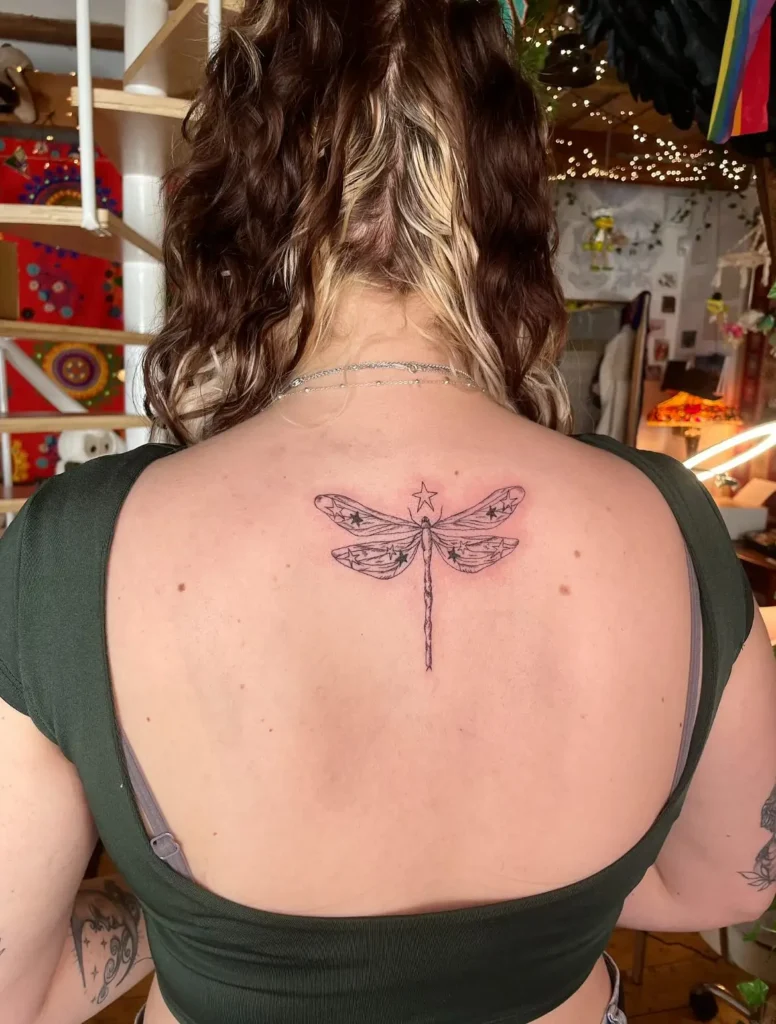 Dragonfly back tattoo with celestial stars and whimsical details, symbolizing wonder and transformation for women

