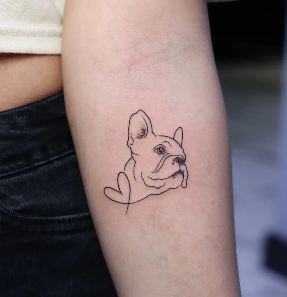 Minimalist line tattoo of a French Bulldog’s face with a heart outline, placed on the upper arm, great for those seeking simple and stylish dog tattoo ideas.