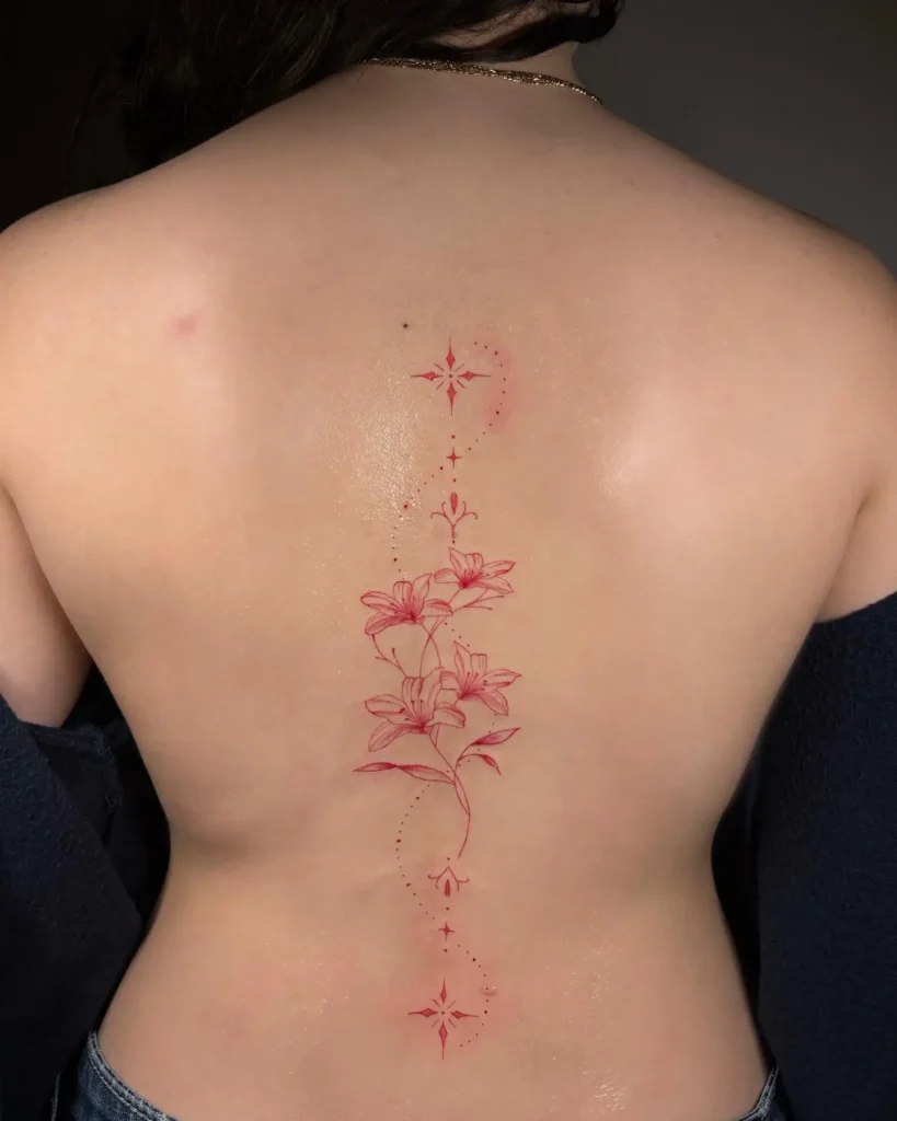 A red ink floral spine tattoo with lilies and star accents running vertically down a woman’s back.