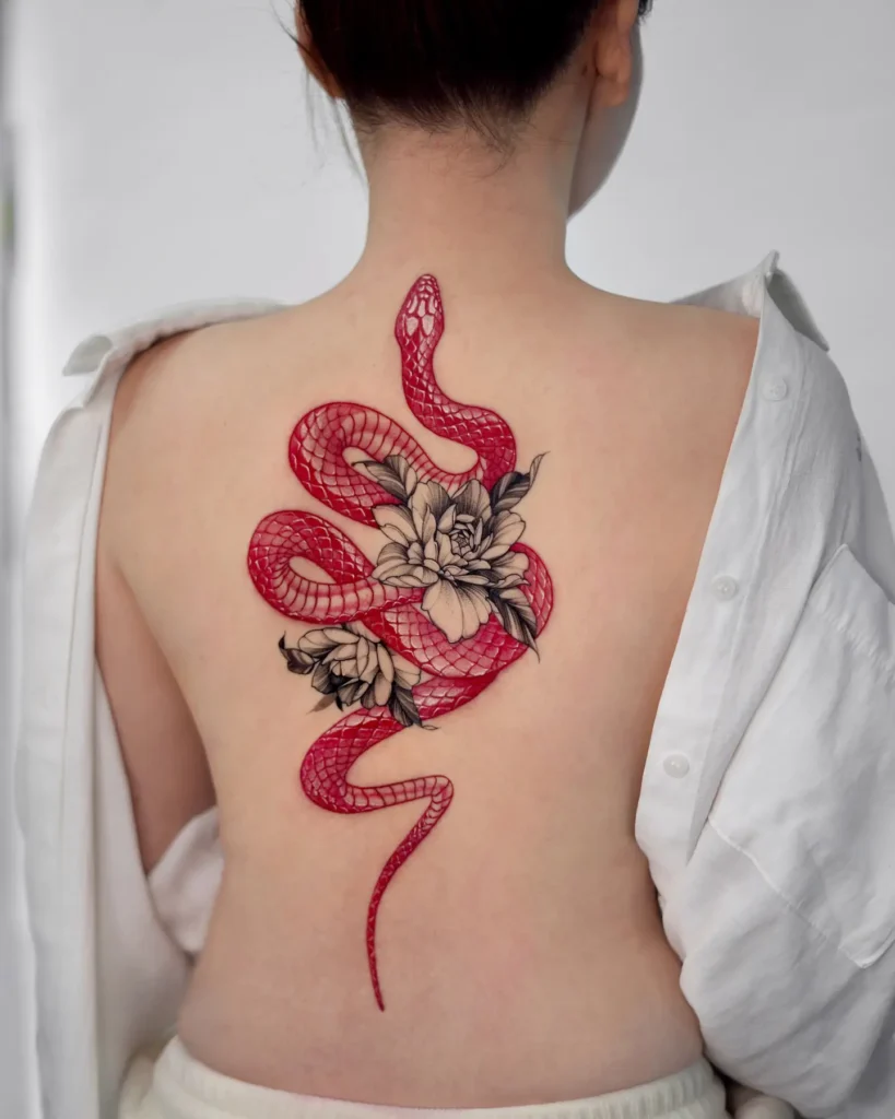 Large red snake tattoo wrapped around black-and-grey flowers on a woman's back. The snake’s scales are vibrant and glossy, while the flowers add soft contrast. Positioned vertically along the spine. Bold and feminine—perfect for animal tattoo ideas simple in theme but dramatic in execution. A strong symbol of rebirth, power, and grace.








