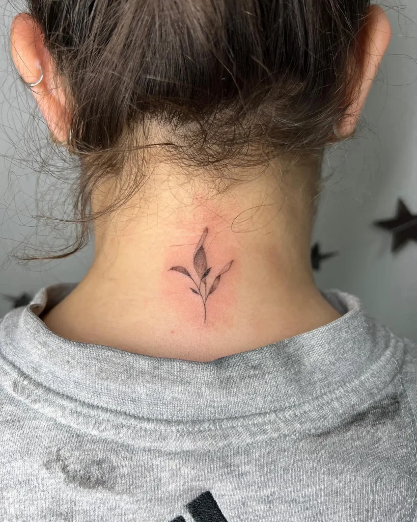 Minimalist back neck tattoo for women featuring a small leaf branch with soft shading at the center of the nape.