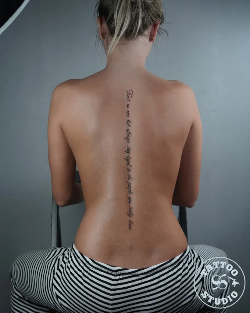 A script spine tattoo featuring an inspirational quote in fine lettering running vertically down a woman’s back.