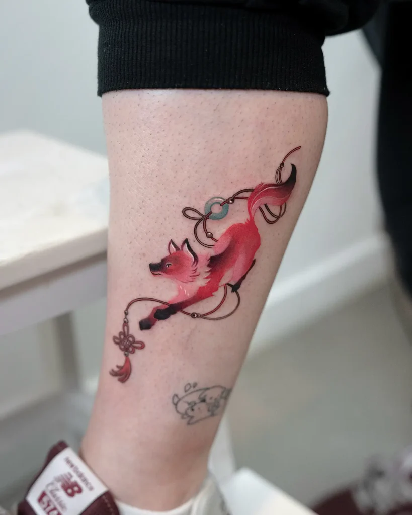 Watercolor-style red fox tattoo with soft black shading and pink undertones, shown mid-leap. Decorated with a floating knot charm and long, flowing ribbons. Placed on the lower leg with a clean, elegant design. A charming choice for animal tattoo ideas simple, inspired by Eastern folklore and symbolism. Represents agility, grace, and good fortune.








