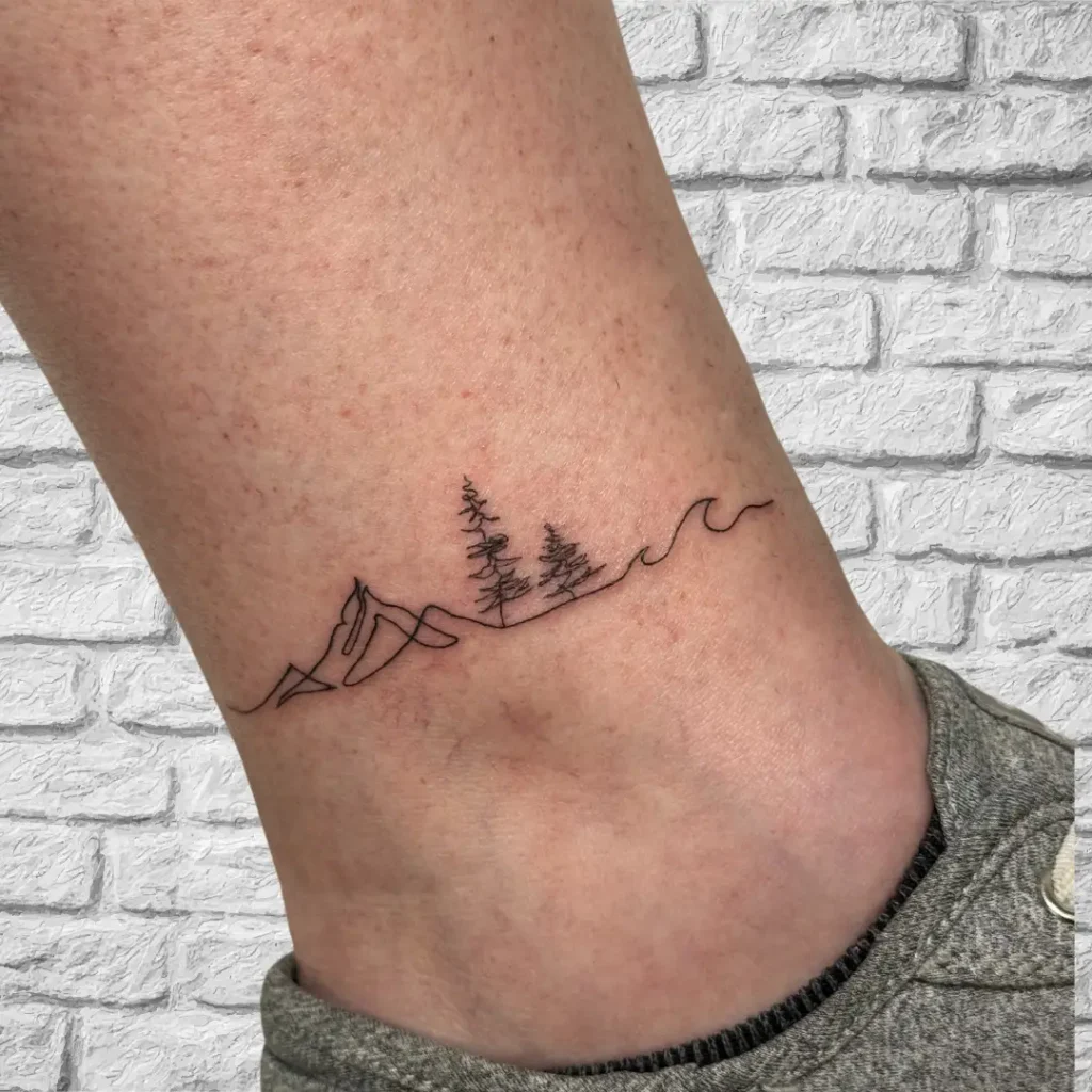 Minimalist continuous line ankle tattoo with mountains, pine trees, and ocean waves, symbolizing nature and balance in a fine line style.
